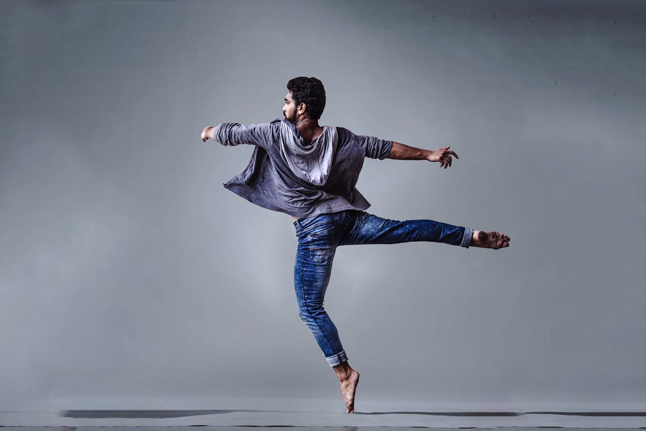 our-mission A male dancer executing a high jump in a studio setting, showcasing grace and agility.